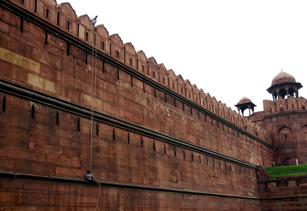 Workers dangling on rope harnesses from the rampart of the Red Fort.