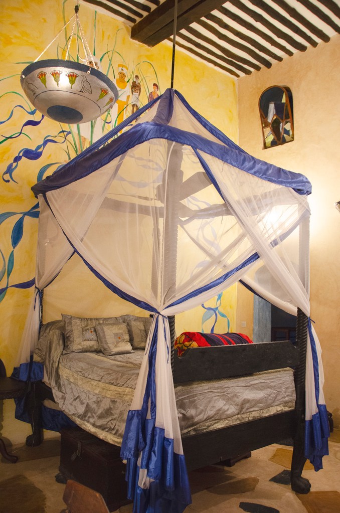 Emerson Spice room interior - Four poster bed with draped netting and walls with mural painting behind.