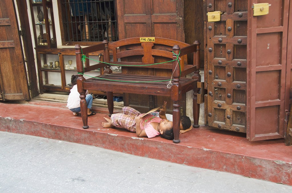 Zanzibar folding door in Gujarati style in a shop and three children at play beneath a wooden bench for sale.